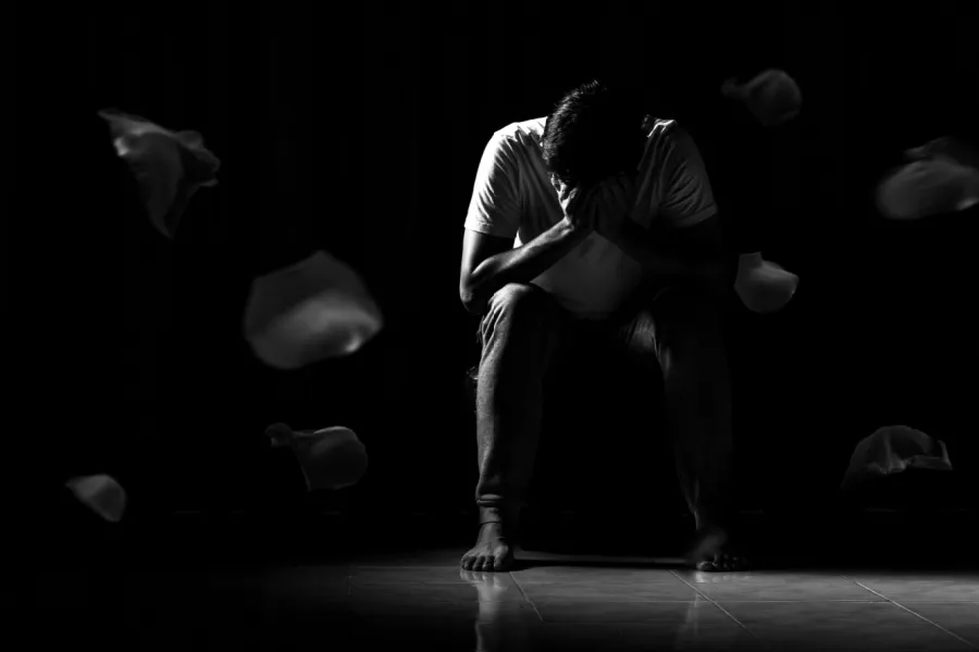 La depresión es hereditaria. Imagen en blanco y negro donde una persona que oculta su cara con las manos se ve al final entre sombras.